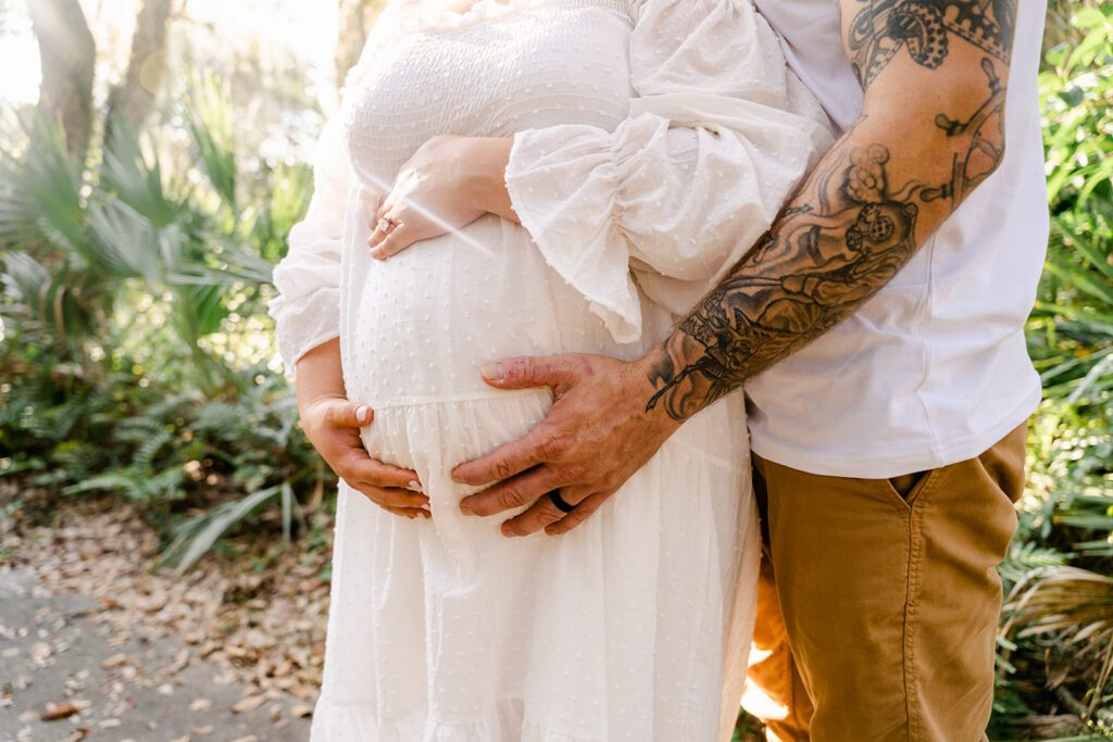 maternity photoshoot in greenery at delray oaks natural area. mom and dads hands are cupping pregnant belly. 