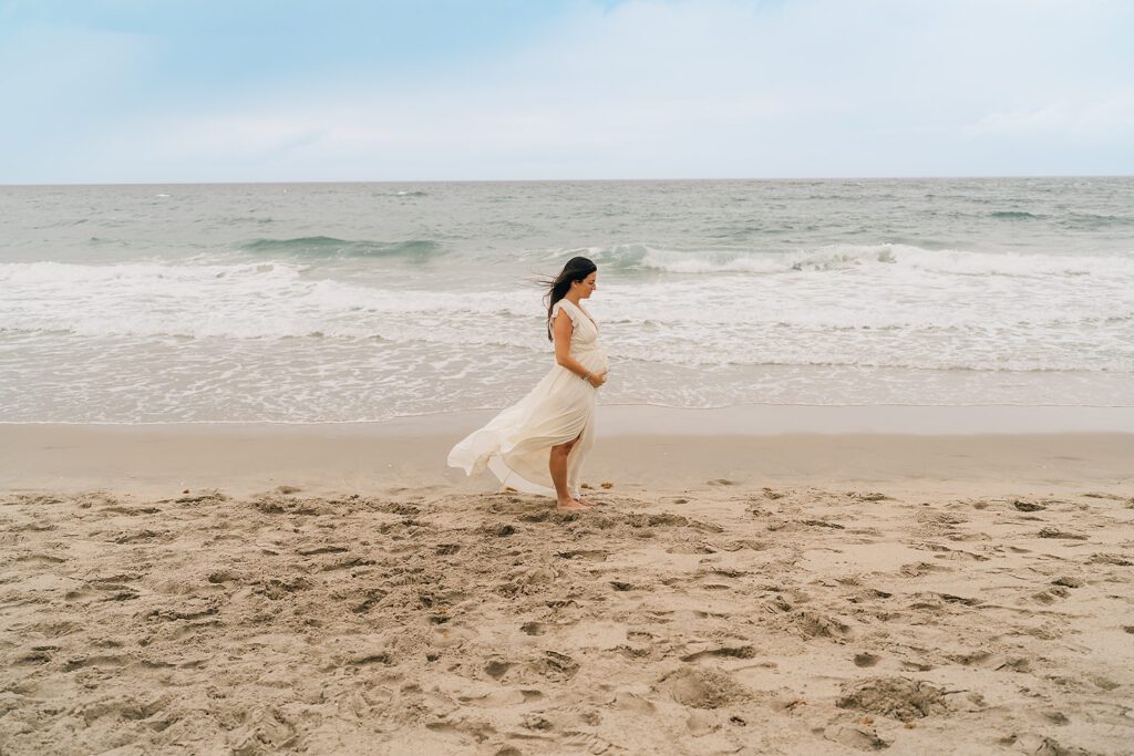 pregnant mother on the beach in a white flowy dress
