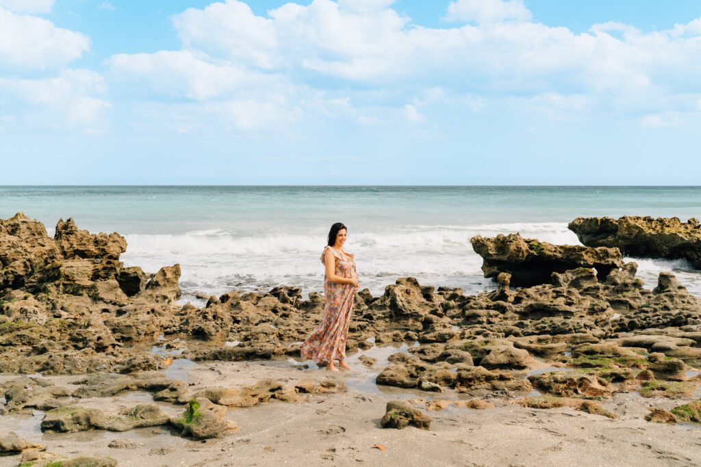 beach maternity photoshoot. pregnant woman in bright dress surrounded by rocks at the beach. 