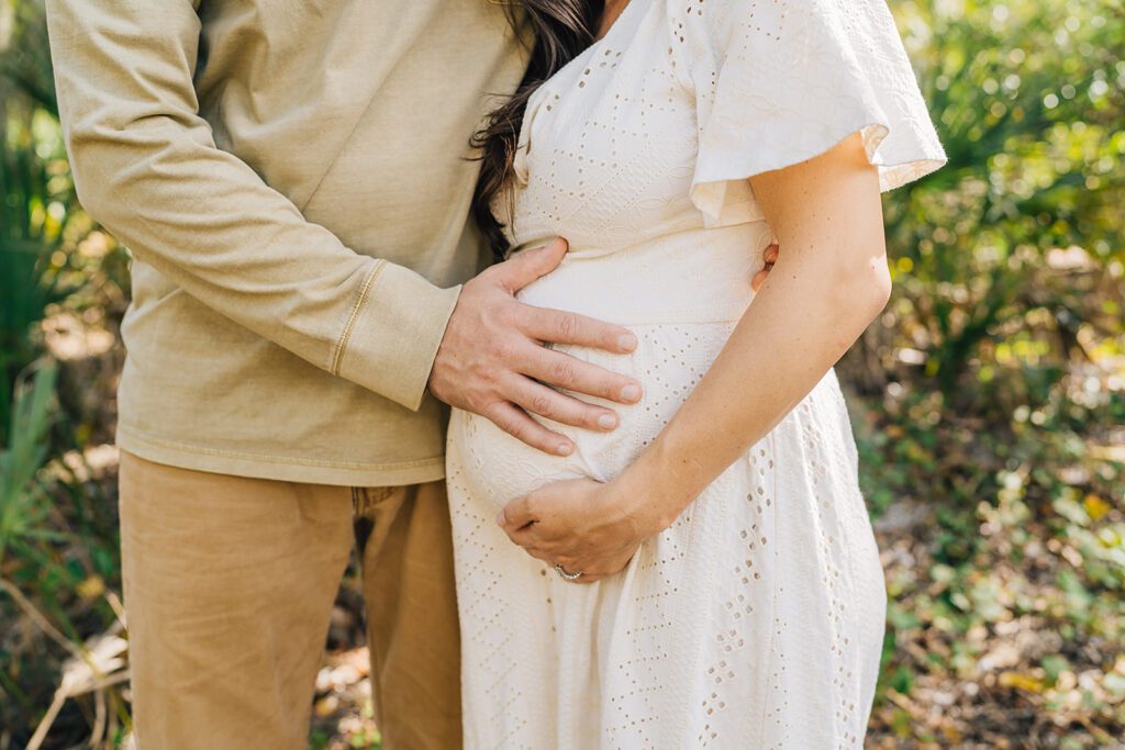 pregnant mom next to dad. both hands on moms belly.